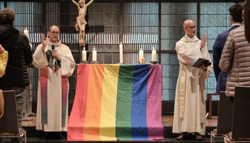 Zwei Geistliche mit Regenbogenfahne und Kreuz im Hintergrund. Ein Gottesdienst für die gleichgeschlechtliche Ehe in der Kirche.