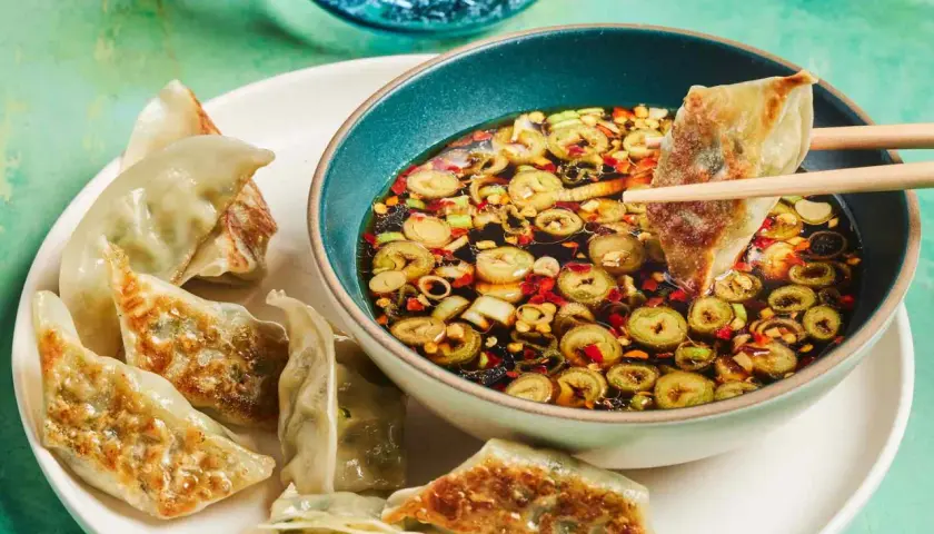 A gyoza is dipped into a flavorful gyoza dipping sauce with scallions and chili flakes.