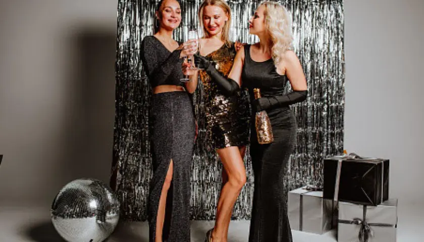 Tres mujeres brindan con copas de champán, luciendo elegantes vestidos para un outfit fin de año mujer.