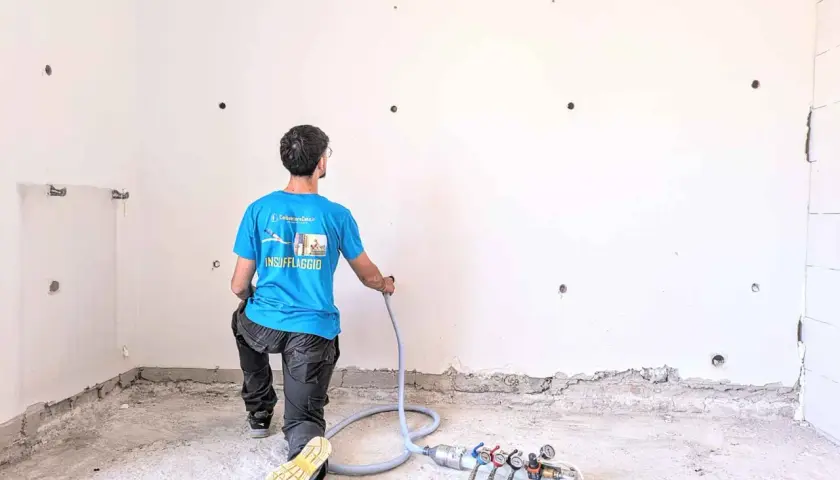 Operaio in ginocchio esegue coibentazione pareti con insufflaggio. Attrezzatura per isolamento termico a terra.