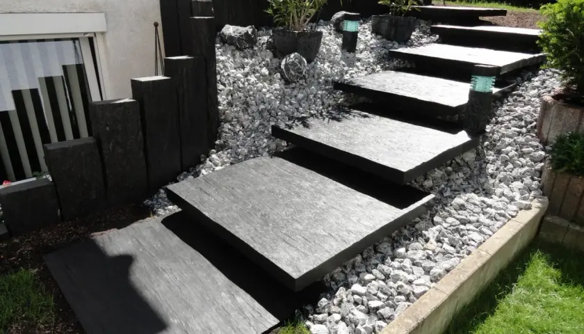 Moderner gartenweg am hang ohne stufen, mit dunklen Steinplatten und Kiesbett.