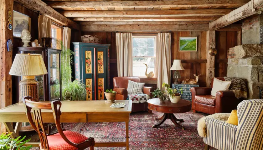 Rustic living room with wooden beams, leather armchairs, a patterned rug, and a vintage cabinet.