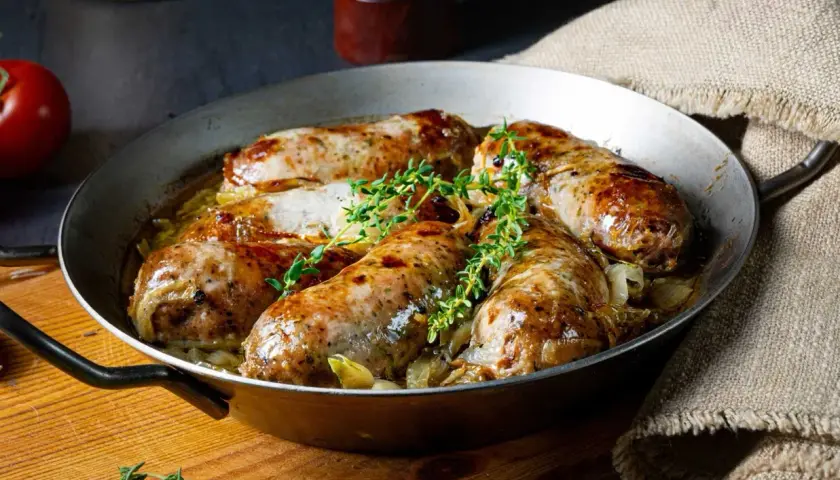 Pieczona biała kiełbasa surowa z cebulą i tymiankiem w metalowej patelni.