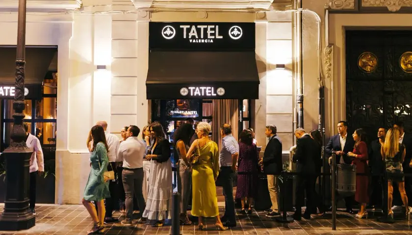 Gente elegante espera en la entrada de Tatel Valencia, un local nocturno iluminado.