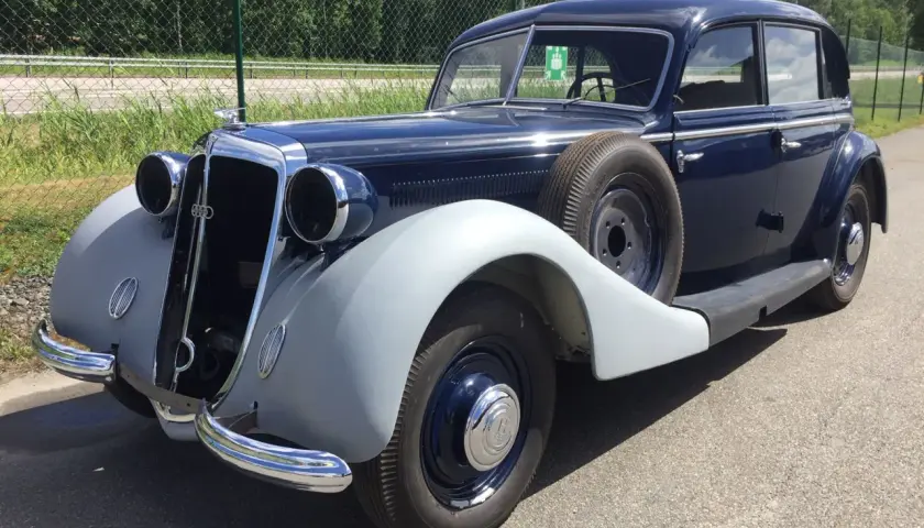 En mörkblå Horsch bil från 1930-talet, med reservhjul monterat på sidan, står parkerad utomhus.