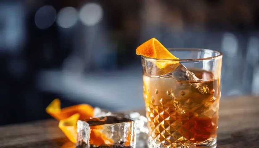 Idealne Old Fashioned w domu: wybór bazy i bittersów. Bursztynowy trunek z lodem i skórką pomarańczy.