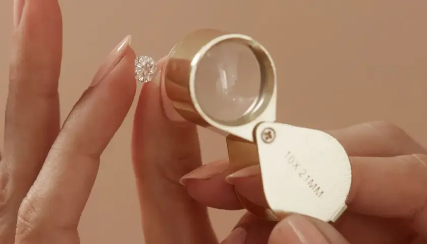 Eine Hand hält einen funkelnden Diamanten, während eine Lupe ihn vergrößert. Ein perfekter einschluss diamant wird genau geprüft.