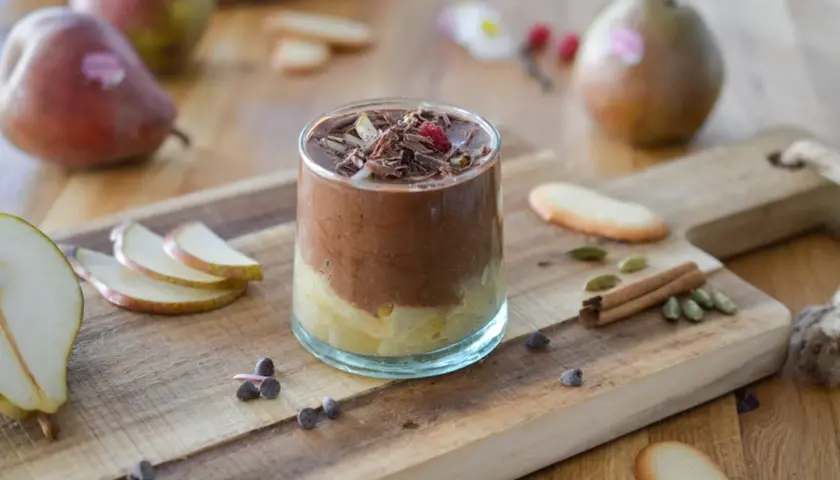 Délicieuse recette mousse poire chocolat, garnie de copeaux de chocolat et d'une framboise. Poires fraîches et épices sur fond de bois.
