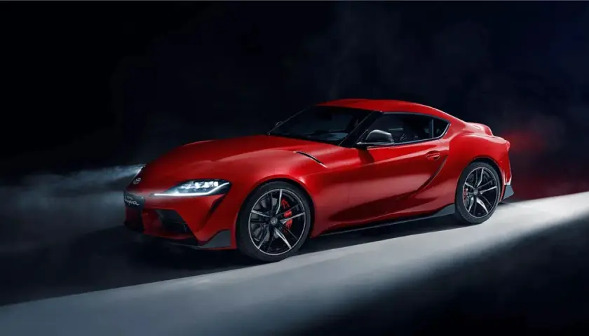 Un deportivo Toyota Supra rojo brillante, con luces encendidas y humo detrás, listo para la acción.