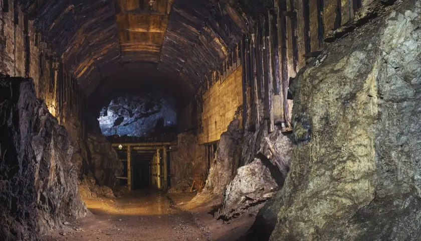 Wnętrze kopalni, drewniane obudowy tunelu, skalne ściany i ciemność. Gdzieś w oddali widać wejście do dalszej części korytarza, jakby otwarta **osowka**.
