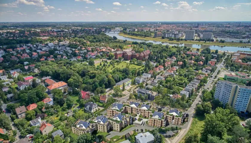 Nowoczesne osiedle w otoczeniu zieleni, z widokiem na rzekę i miasto. W oddali widać zabytkowe budynki i nowe apartamentowce. To idealne miejsce dla osób ceniących spokój i bliskość natury, a jednocześnie dostęp do miejskich atrakcji.