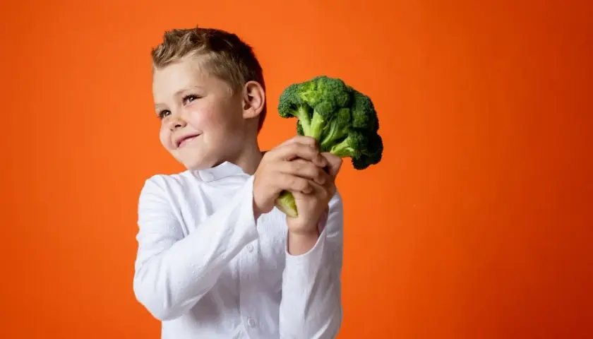 Bambino sorridente con un broccolo, un ortaggio salutare. Non è un legume, ma è ottimo per la salute!