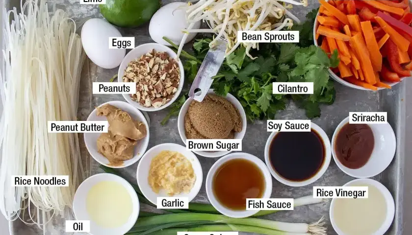 Składniki do pad thai: makaron ryżowy, jajka, orzeszki ziemne, masło orzechowe, olej, czosnek, zielona cebulka, kiełki fasoli, kolendra, cukier brązowy, sos sojowy, sos rybny, ocet ryżowy, sriracha, marchewka i papryka.