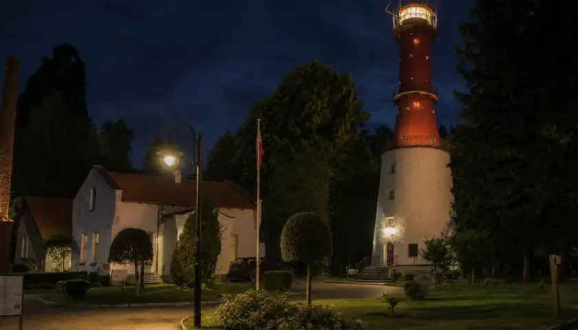 Latarnia morska Jastrzębia Góra nocą, z oświetlonym budynkiem i charakterystyczną czerwoną wieżą.
