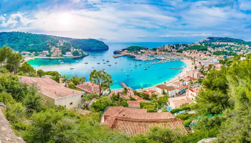 Bahía turquesa con barcos y casas en laderas verdes, un paraíso que evoca **islas secretas** y tranquilidad.