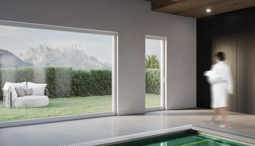 Interno moderno con piscina, grandi vetrate che incorniciano montagne e giardino, e infissi in legno lamellare che creano un'atmosfera calda.