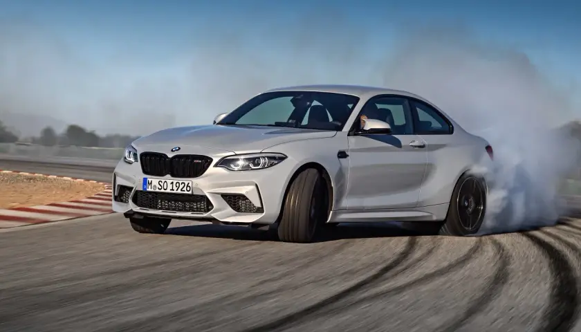 Un BMW M2 Competition CV derrapa en una pista, dejando estelas de humo y marcas de neumáticos.