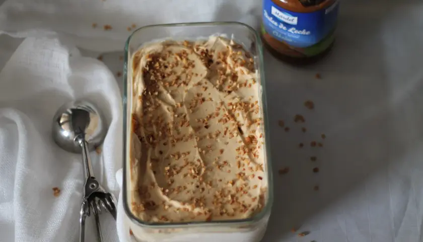 Gelato cremoso con granella di nocciole, accanto a un barattolo di dulce de leche.