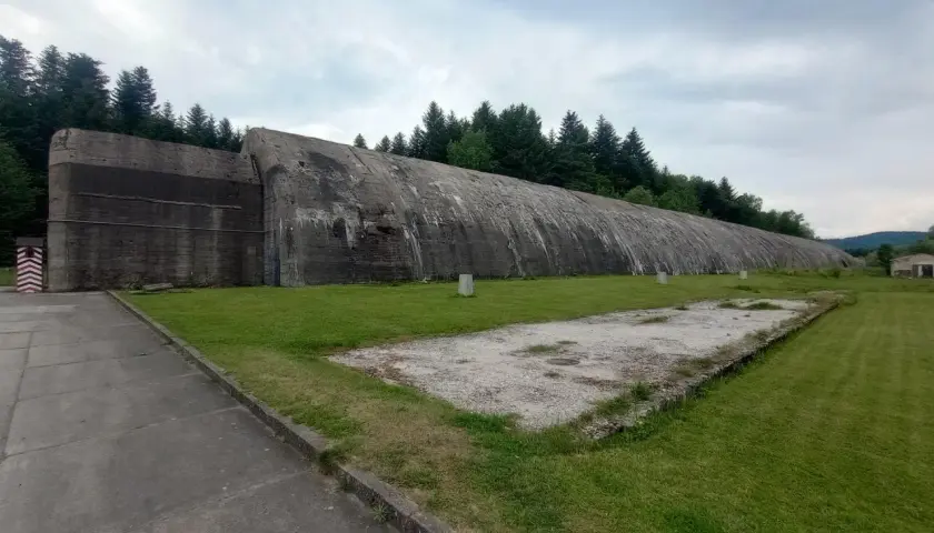 Ogromny betonowy bunkier w Frysztaku, otoczony zielenią i lasem.