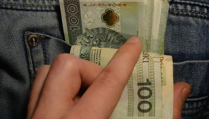 Dłoń wyciąga banknoty 100 zł z kieszeni dżinsów. Może to symbolizować walkę z zatorami płatniczymi lub po prostu gotówkę.