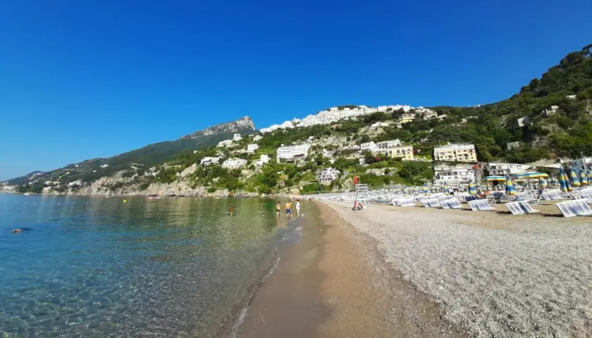 Plage de galets à Vietri sul Mare, Italie, avec des maisons blanches perchées sur la colline verdoyante et la mer bleue étincelante.