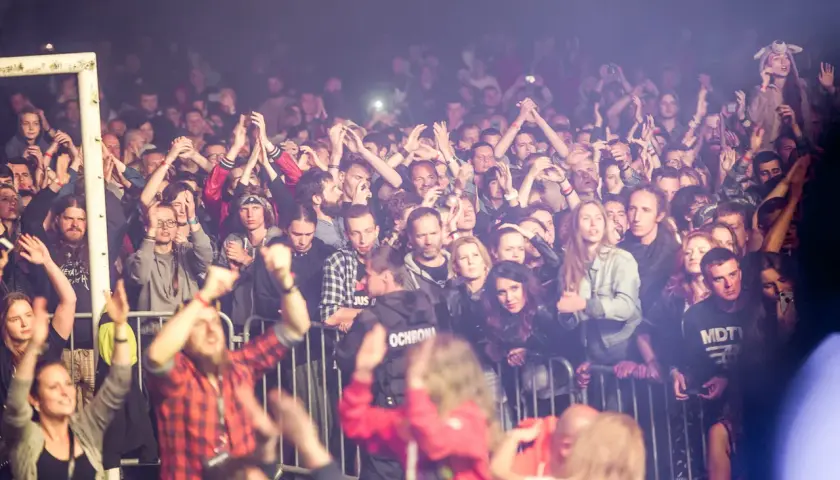 Tłum ludzi na festiwalu w Bieszczadach, z rękami w górze, cieszący się muzyką.