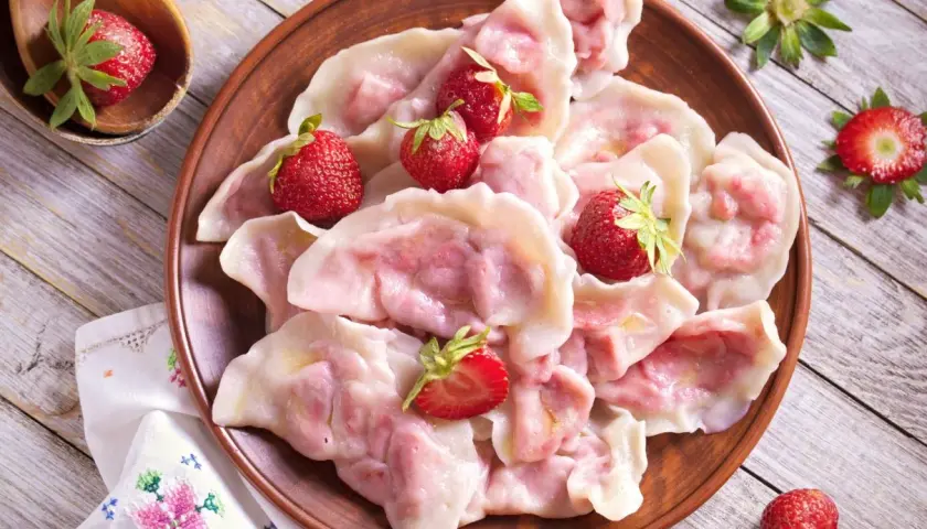 Pyszne pierogi z truskawkami, ozdobione świeżymi owocami, wyglądają apetycznie na glinianym talerzu.