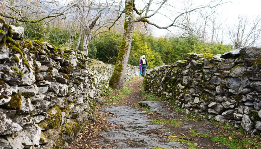 Sendero de piedra cubierto de musgo, parte de la ruta Garganta de Escuain. Dos excursionistas avanzan por el camino.