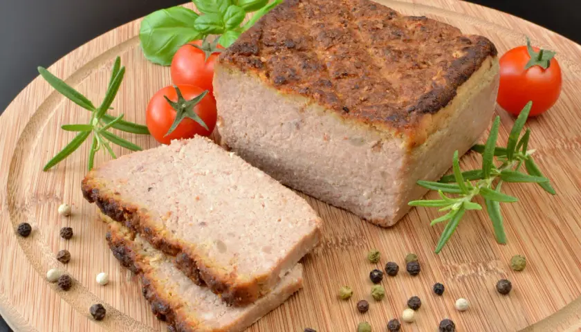 Upieczony pasztet na desce z pomidorkami, rozmarynem i pieprzem.
