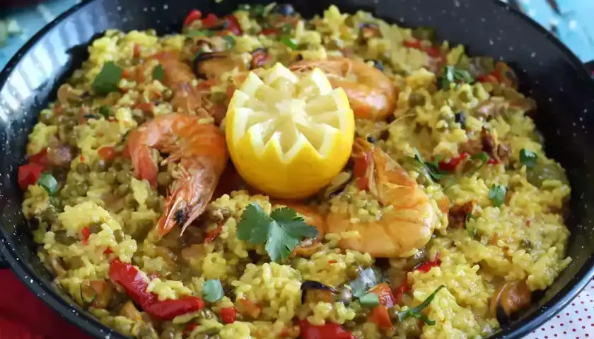 Arroz con pollo y marisco en paellera, adornado con limón y perejil. Un festín de sabores.