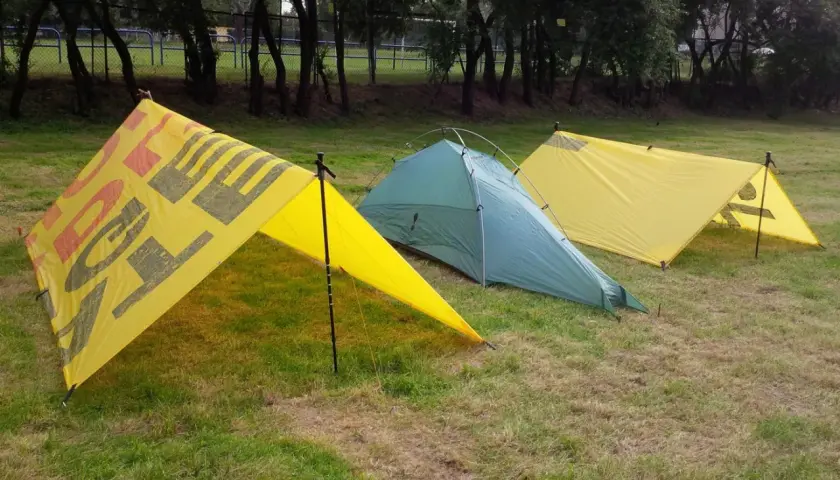 Trzy namioty na trawie. Dwa żółte z napisem "OUTDOOR" i jeden zielony. Namiot z tarpa gotowy na przygodę.