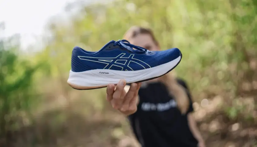 Dłoń trzymająca niebieski but Asics z białym logo. Idealna rozmiarówka Asics dla biegaczy.