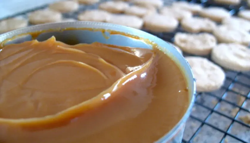 Un pot de confiture de lait onctueuse, prêt à garnir des biscuits secs disposés sur une grille.