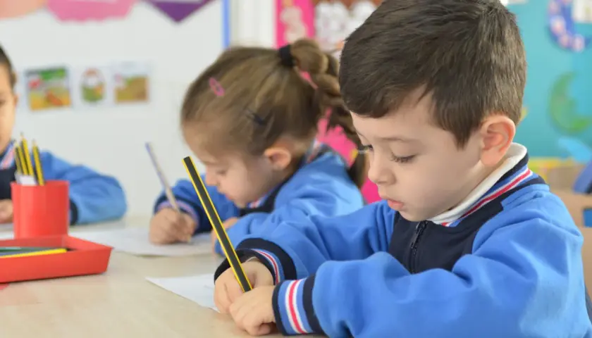 Niños concentrados en sus cuadernos, un momento de aprendizaje y adaptación en el aula.