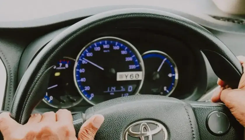 Ręce na kierownicy Toyoty, widoczne zegary i wskaźniki. Elektryczne wspomaganie kierownicy ułatwia jazdę.