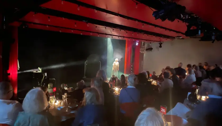 En föreställning på soppteatern Stockholm. En ensam artist står på scenen i strålkastarljus, publiken sitter vid dukade bord.