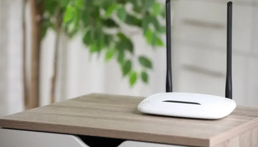 Biały router z dwiema antenami na drewnianym blacie. Dowiedz się, jak działa router bez karty SIM, tworząc domową sieć Wi-Fi.