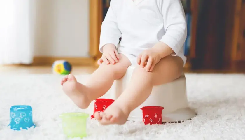Liten bebis på pottan, redo att sluta med napp. Färgglada leksaker och en mjuk matta skapar en trygg miljö för potträning.