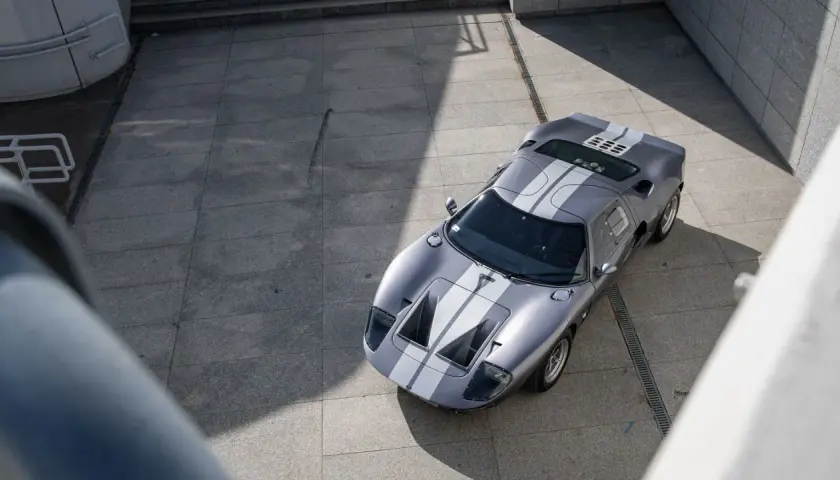 Srebrny Ford GT40 z białymi pasami, gotowy do wyścigu. Ikona motoryzacji na betonowym placu.