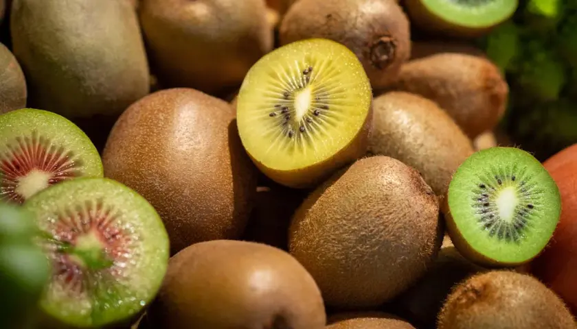 Ein Haufen Kiwis, einige ganz, andere aufgeschnitten, zeigen ihr grünes und gelbes Fruchtfleisch. Gut für den Schlaf, da sie Melatonin enthalten.
