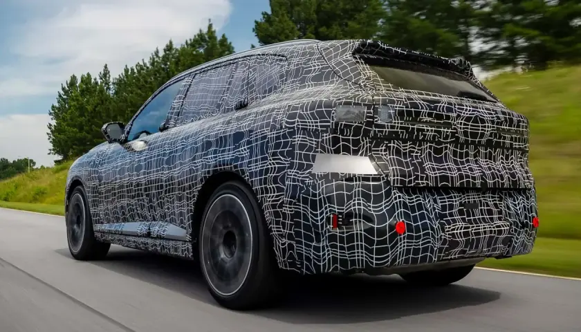 La nuova BMW X5 2026, con la sua mimetica di test, sfreccia su una strada panoramica, anticipando il futuro del design.