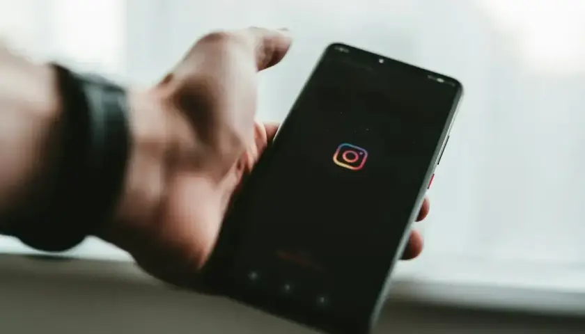 Dłoń trzyma smartfon z logo Instagram. Chcesz wiedzieć, jak zobaczyć relacje na IG?