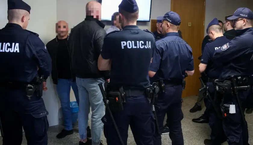 Policjanci otaczają grupę mężczyzn, wśród których mogą być psycho fans. Wszyscy mają zakryte twarze.