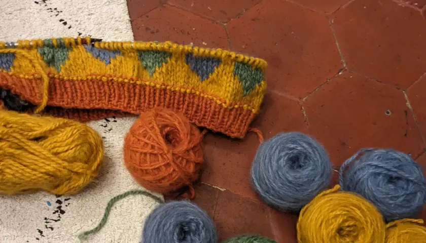 Un tricot jacquard aux motifs géométriques colorés, entouré de pelotes de laine.