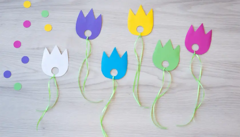 Bunte Papier-Tulpen mit grünen Bändern, perfekt für das Basteln mit Kindern. Bunte Tupfen liegen verstreut.