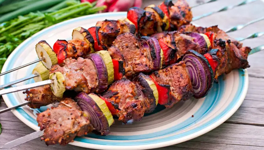 Brochettes d'agneau grillées avec oignons rouges, poivrons et courgettes sur une assiette bleue et blanche.