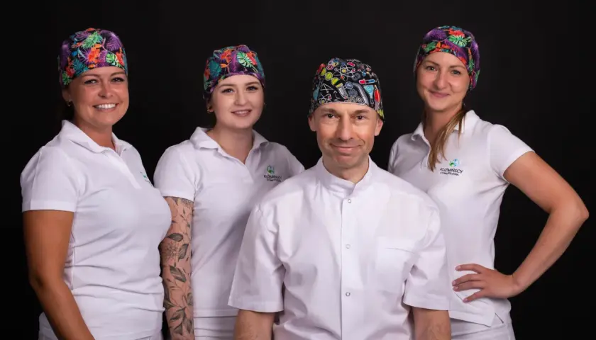 Cztery osoby w białych uniformach i kolorowych czepkach stomatologicznych na czarnym tle.