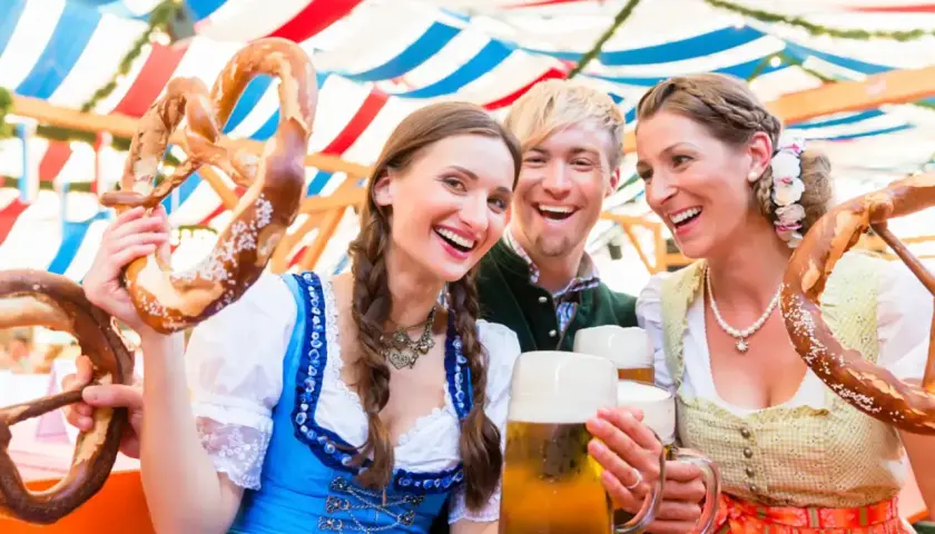 Trois amis joyeux célèbrent à l'Oktoberfest, un lieu festif, avec des bretzels géants et de la bière.