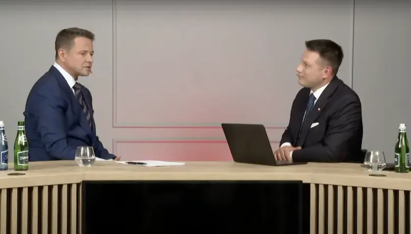 Sławomir Mentzen w garniturze siedzi przy biurku z laptopem, rozmawiając z drugim mężczyzną. Czy to dowód, dlaczego Sławomir Mentzen unika debat z kandydatami Koalicji Obywatelskiej?