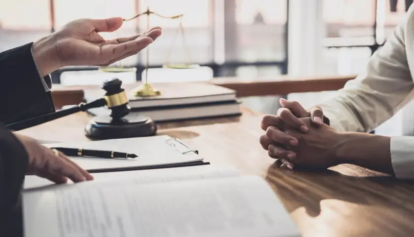 Prawnik omawia z klientem formalności związane z wnioskiem o stwierdzenie nabycia spadku. Na stole leżą dokumenty, młotek sędziowski i waga sprawiedliwości.